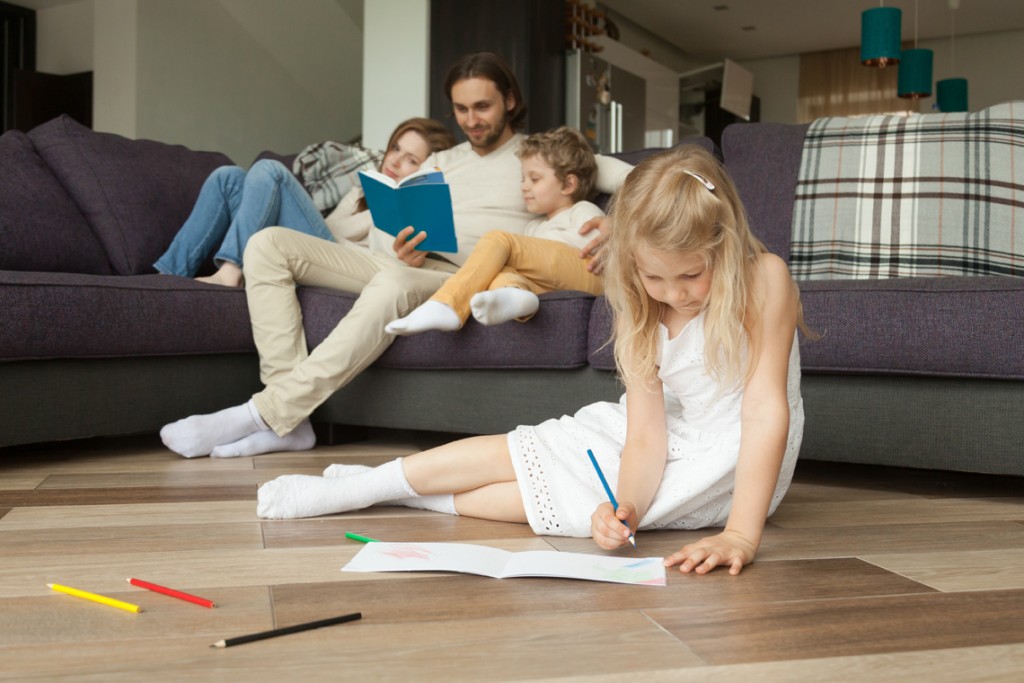 Daughter playing on floor while parents and son reading book